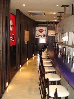 白い椅子が並ぶカウンター席と、赤い暖簾のかかる店内