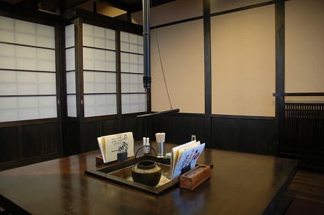 障子と黒い梁に囲まれた囲炉裏風の座敷席。鉄瓶とお品書きが置かれたテーブル。