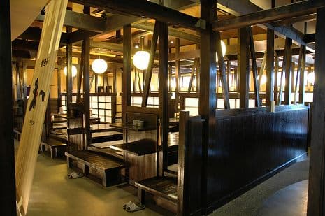 丸い照明が灯る掘りごたつ席。黒い梁と木の温もりが感じられる空間